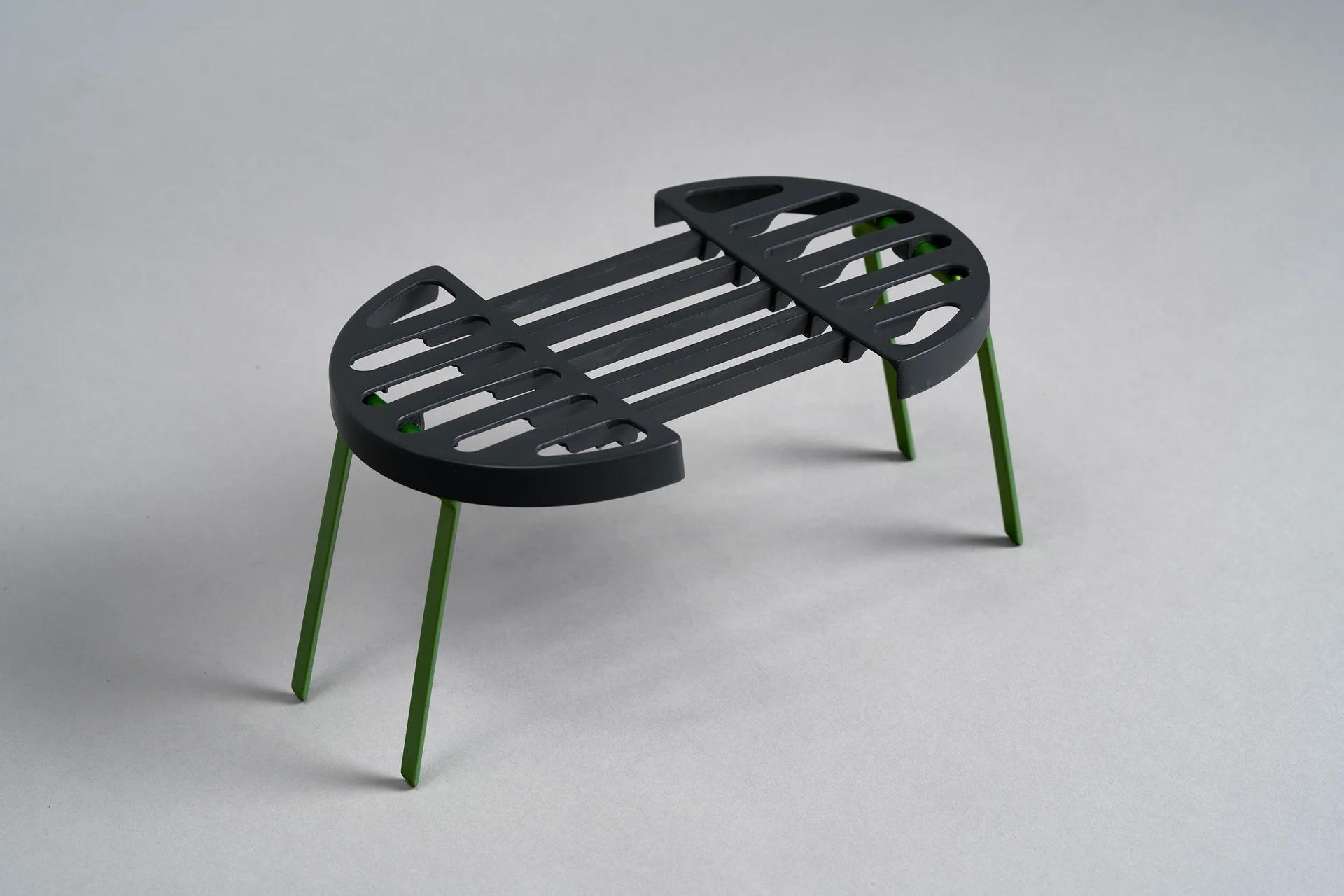 Folded A.O.K. grill with green legs on a grey background