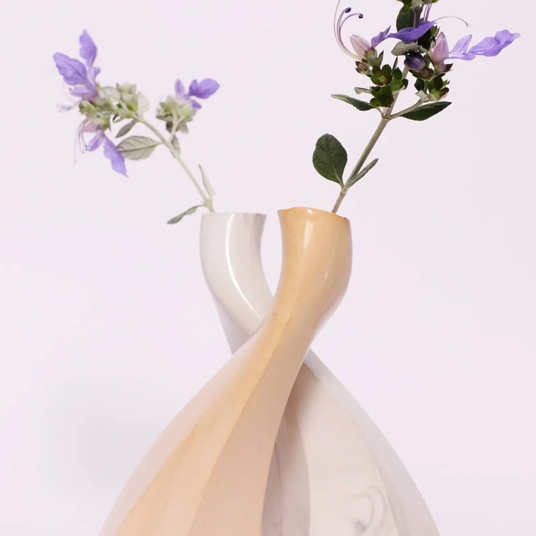Two ceramic vases twisting around each other, holding flowers
